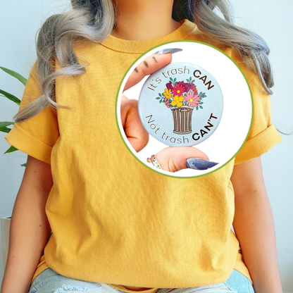 Person wearing a yellow t-shirt and light blue jeans, with a circular inset displaying the "It's trash CAN Not trash CAN'T" button pin being held up close.